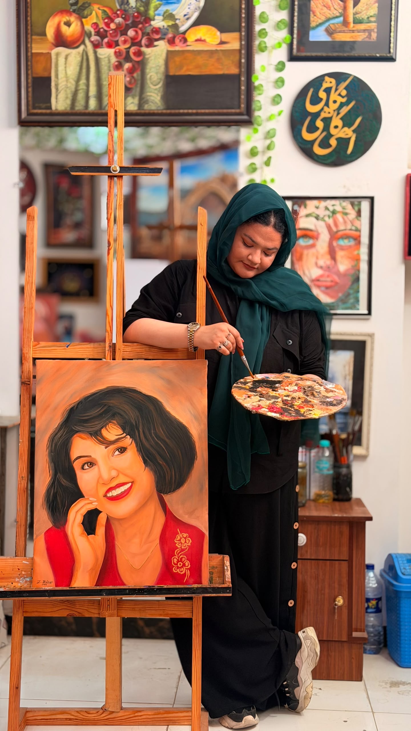 Zuhra standing beside her easel and painting a portrait in her studio
